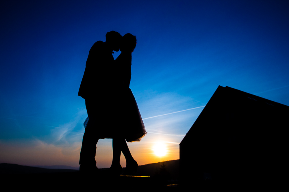 Novomanželé v objetí při západu slunce.